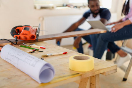 selective focus of wooden table with blueprint and couple sitting behind during renovation at homeの写真素材