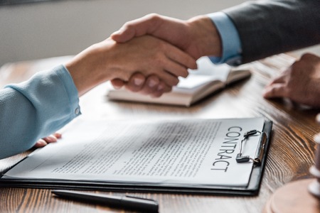 close-up view of clipboard with contract and lawyer with client shaking hands behind