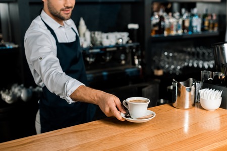 cropped view of barista in apron putting coffee cup at wooden counterの写真素材