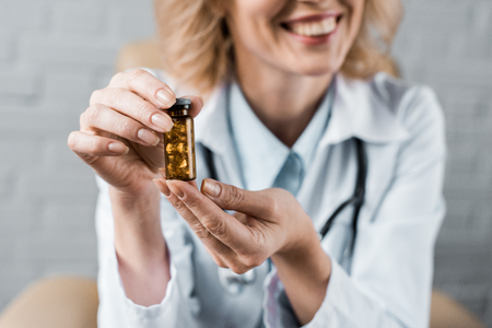 cropped shot of smiling female doctor showing jar of pills to patient at officeの写真素材