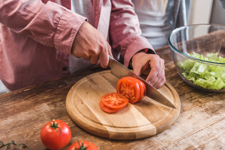 Cropped view of man cutting tomato on wooden board in kitchenの写真素材