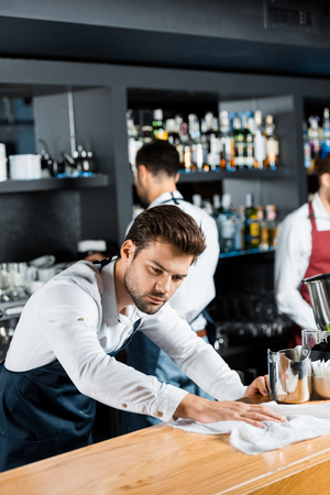 adult concentrated barman cleaning wooden counter with clothの写真素材