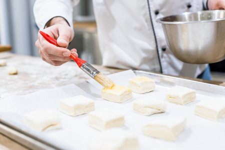 Male hand of chef oiling dough with basting brush in kitchenの写真素材