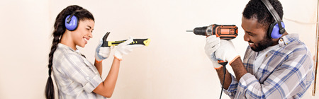 side view of couple in protective headphones having fun with tools during renovation of home