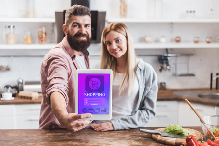smiling couple holding digital tablet with online shopping app on screenの写真素材
