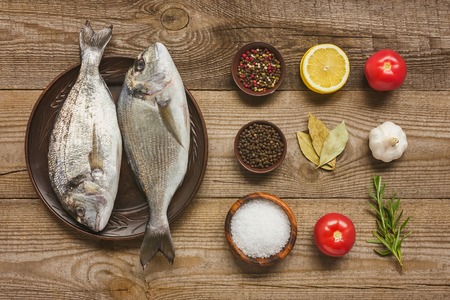 view from above of plate with uncooked fish near arranged ingredients on wooden tableの写真素材