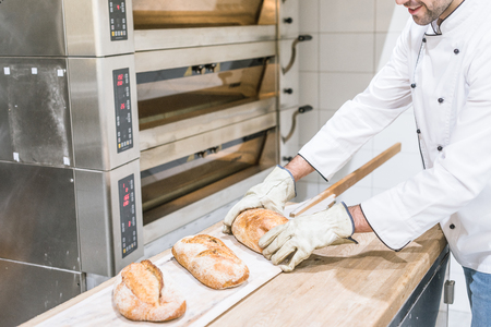 baker standing near oven with hot baked bread on wooden counterの写真素材