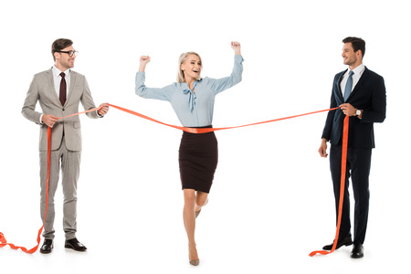 excited businesswoman reaching finishing line while businessmen holding red ribbon isolated on whiteの写真素材