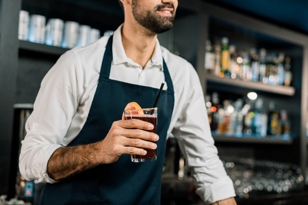 Bartender standing in apron with cocktail in glassの写真素材
