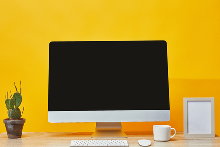 Computer, cactus in pot and cup of coffee at wooden table on yellowの写真素材