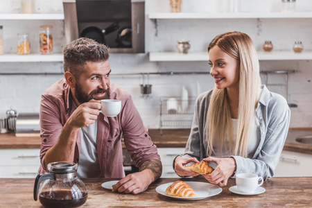 young cheerful couple eating croissants and drinking coffee for breakfastの写真素材