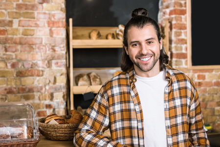 Handsome seller smiling and standing in bakeryの写真素材
