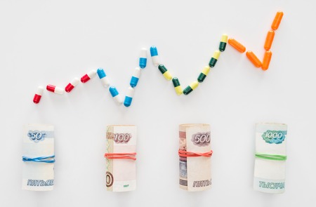 top view of graph of colorful pills and rolled russian banknotes placed in row on white surfaceの写真素材