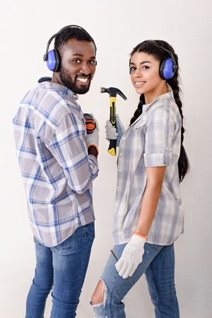happy young couple with protective headphones and tools looking at camera while making renovation of homeの写真素材