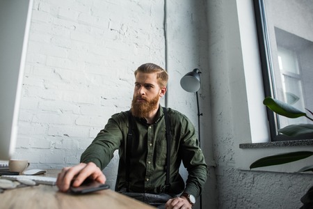 businessman holding smartphone at table and looking away