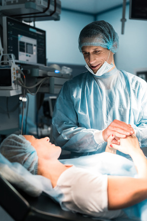 smiling doctor and patient holding hands in surgery roomの写真素材