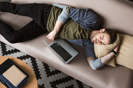 high angle view of overworked man with laptop sleeping on couchの写真素材