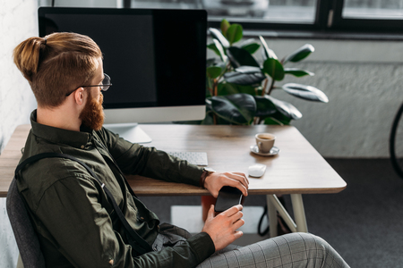 handsome businessman holding smartphone and looking awayの写真素材