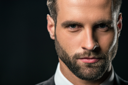 portrait of handsome businessman in jacket looking at camera, isolated on blackの写真素材