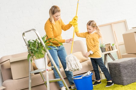 mother and daughter holding mop and cleaning room after relocationの写真素材