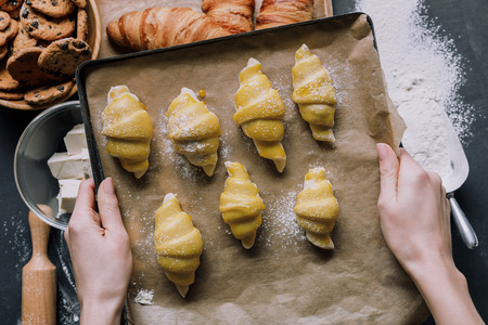 partial view of woman holding tray with dough for croissants over table ingredientsの写真素材