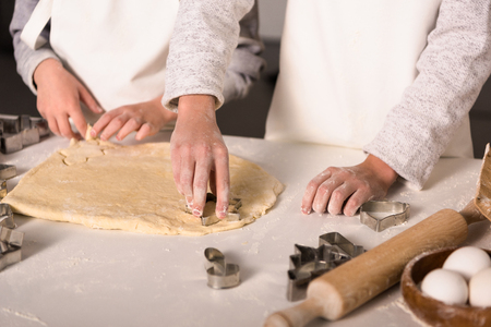 partial view of children in aprons cutting out dough for cookies at table in kitchenの写真素材