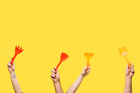 cropped shot of male and female hands holding red and yellow plastic shovels and rakes isolated on...