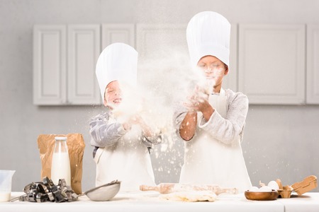 happy children in chef hats having fun with flour in kitchen