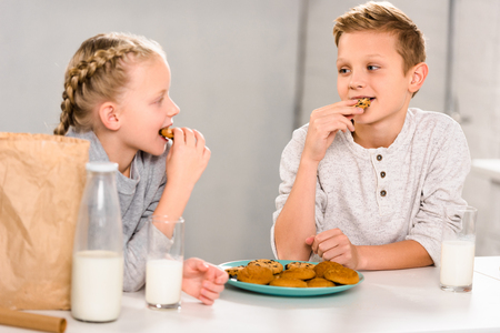 happy children eating cookies and drinking milk at table in kitchenの写真素材
