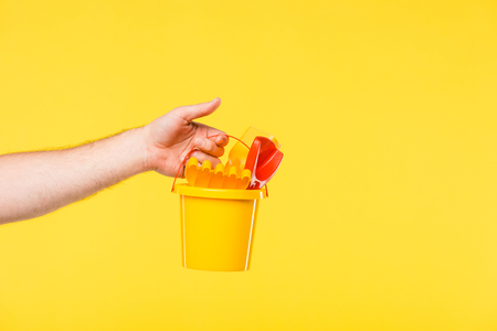 cropped shot of person holding plastic bucket with toys isolated on yellowの写真素材