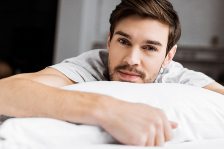 handsome young man lying on bed and looking at cameraの写真素材