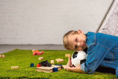 adorable boy laying with soccer ball on green lawn at homeの写真素材