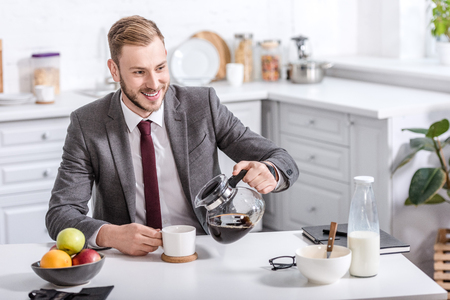 handsome businessman pouring filtered coffee in cup at kitchen tableの写真素材