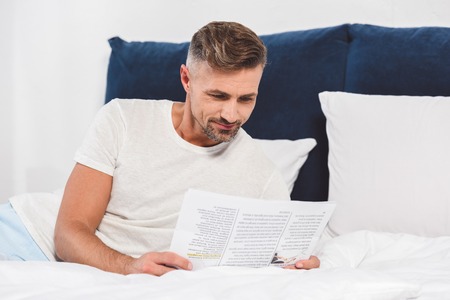 Handsome man reading newspaper in bedの写真素材