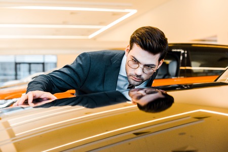concentrated businessman in eyeglasses choosing automobile in dealership salonの写真素材