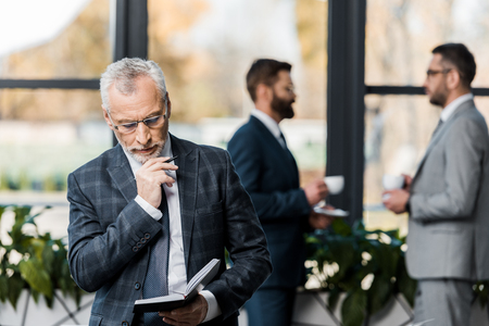 concentrated mature businessman holding pen and notepad in officeの写真素材