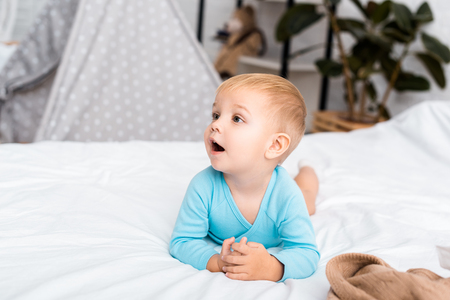 cute child in blue bodysuit lying on stomach in bedの写真素材