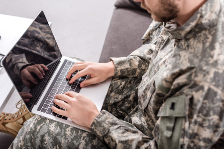 partial view of army soldier using laptop on couchの写真素材