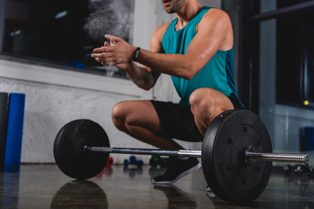 cropped view of sportsman with talcum powder training with barbell in gym