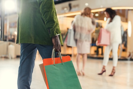 cropped shot of african american man holding paper bags while walking in shopping mallの写真素材