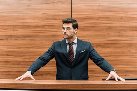 confident young businessman in eyeglasses standing at reception of modern office