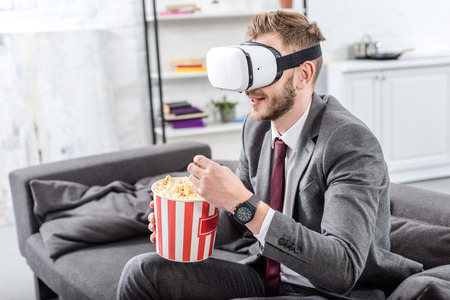 businessman on couch in virtual reality headset watching movie and eating popcorn