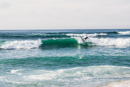 unidentified surfer on surfboard riding wave and beautiful seascape at cloudy day, Portugalの写真素材