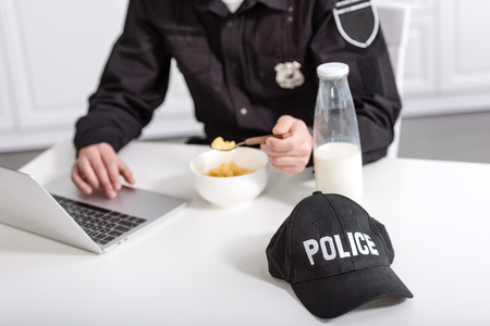 cropped view of police officer using laptop and eating cornflakes at kitchen tableの写真素材