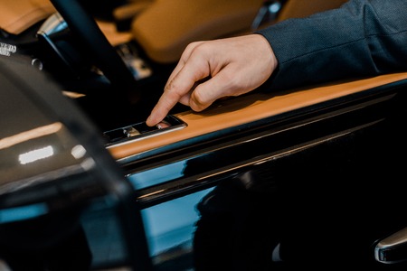 cropped image of businessman pushing button for closing window of automobile
