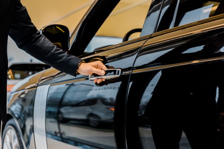 cropped image of businessman in suit opening door of black automobileの写真素材