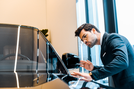 young handsome businessman in eyeglasses choosing car in dealership salonの写真素材