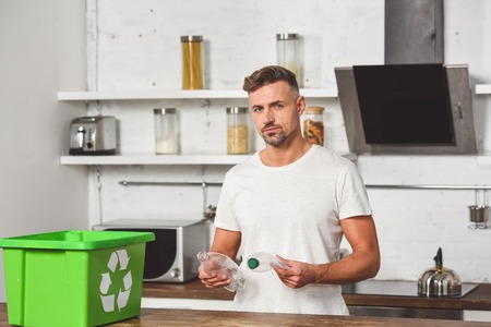 handsome man holding plastic bottles with green recycle box at wooden table
