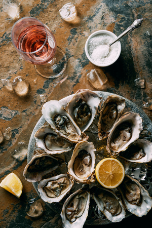 Flat lay with glass of wine, oysters with ice and lemon pieces on grungy tabletopの写真素材