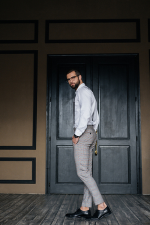 Fashionable elegant man posing in white shirt and suspenders against door in loft interiorの写真素材